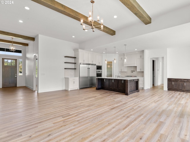 kitchen with built in appliances, a center island with sink, beamed ceiling, and light hardwood / wood-style floors