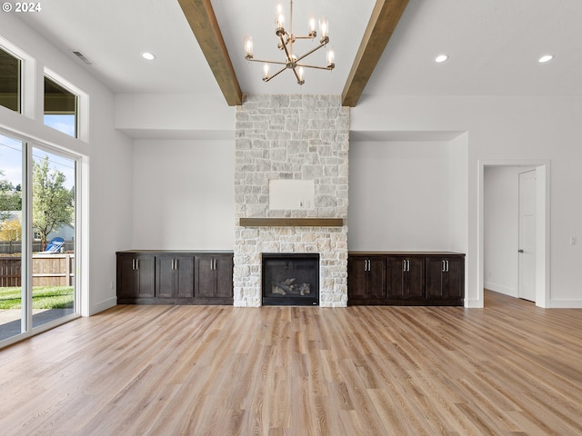 unfurnished living room featuring a notable chandelier, beam ceiling, a stone fireplace, and light wood-type flooring