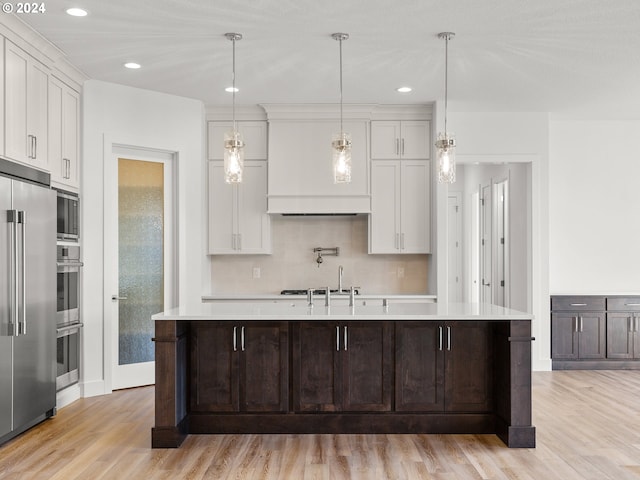 kitchen featuring white cabinets, light wood-type flooring, and an island with sink