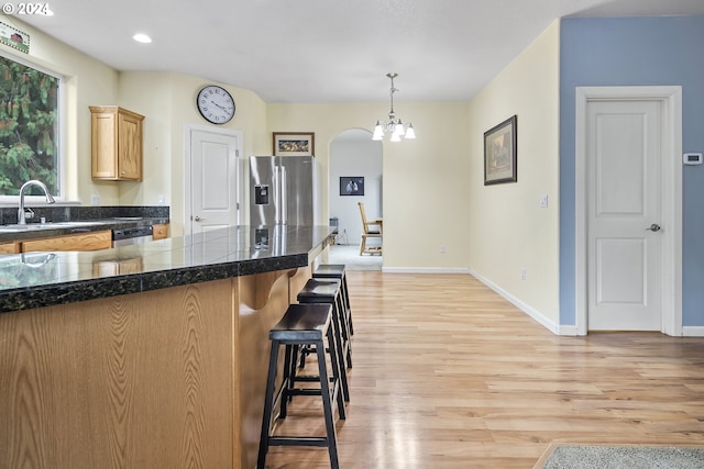 kitchen with appliances with stainless steel finishes, a kitchen breakfast bar, pendant lighting, a notable chandelier, and light hardwood / wood-style flooring