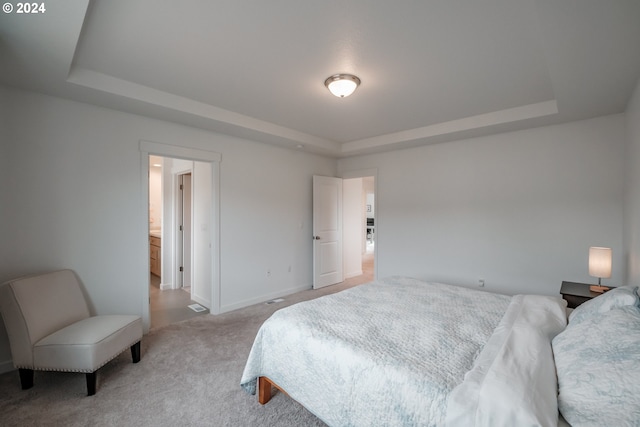 bedroom with ensuite bath, a tray ceiling, and light carpet