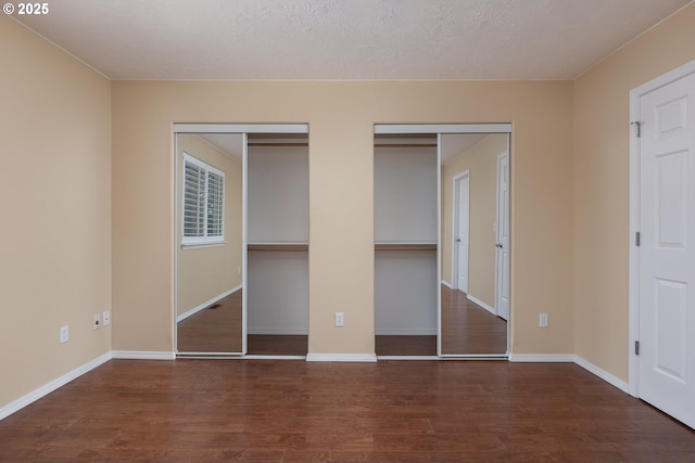 unfurnished bedroom with wood finished floors, baseboards, two closets, and a textured ceiling