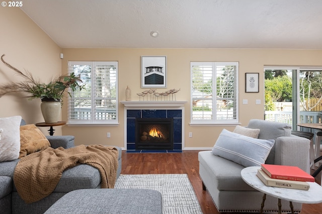 living room with baseboards, lofted ceiling, wood finished floors, and a tile fireplace