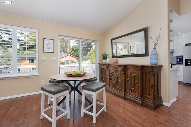 dining space featuring wood finished floors, baseboards, and vaulted ceiling