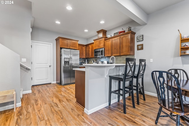 kitchen featuring kitchen peninsula, a kitchen bar, appliances with stainless steel finishes, light hardwood / wood-style floors, and tasteful backsplash