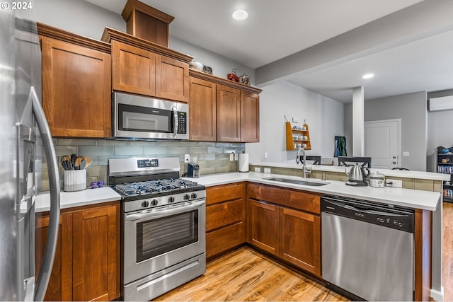 kitchen with appliances with stainless steel finishes, sink, kitchen peninsula, light hardwood / wood-style floors, and decorative backsplash