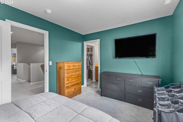 bedroom with a textured ceiling, a walk in closet, a closet, and light colored carpet