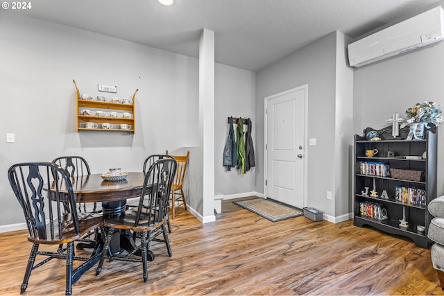 dining space with a wall mounted air conditioner, a textured ceiling, and wood-type flooring