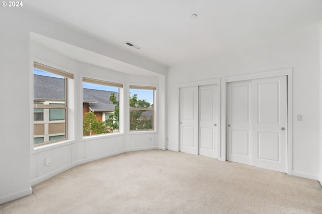 unfurnished bedroom with light carpet and two closets