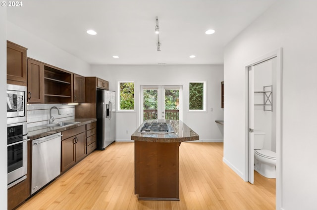 kitchen featuring dark countertops, appliances with stainless steel finishes, a center island, open shelves, and a sink