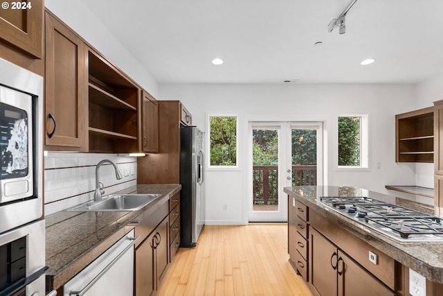 kitchen with track lighting, stainless steel appliances, backsplash, sink, and light hardwood / wood-style floors