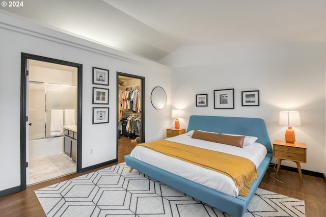 bedroom with ensuite bath, vaulted ceiling, dark wood-type flooring, a spacious closet, and a closet