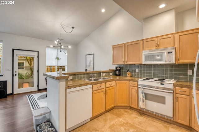 kitchen featuring white appliances, high vaulted ceiling, an inviting chandelier, sink, and kitchen peninsula