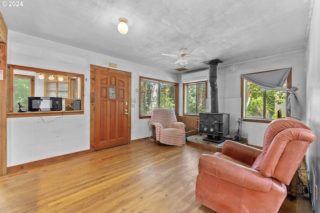 living room featuring light wood-style floors, an AC wall unit, baseboards, and a wood stove