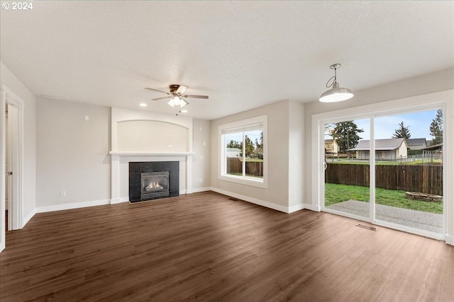 unfurnished living room with ceiling fan, dark hardwood / wood-style flooring, a textured ceiling, and a tiled fireplace