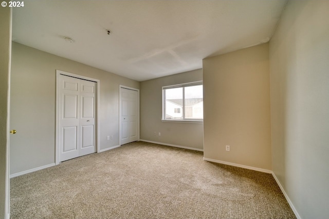 unfurnished bedroom featuring light colored carpet and multiple closets