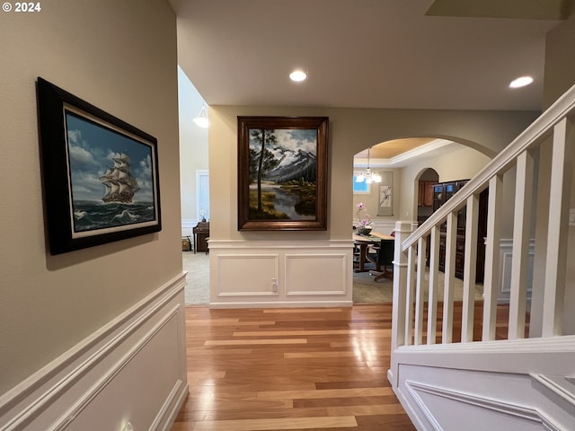 hallway with an inviting chandelier, crown molding, and light hardwood / wood-style floors