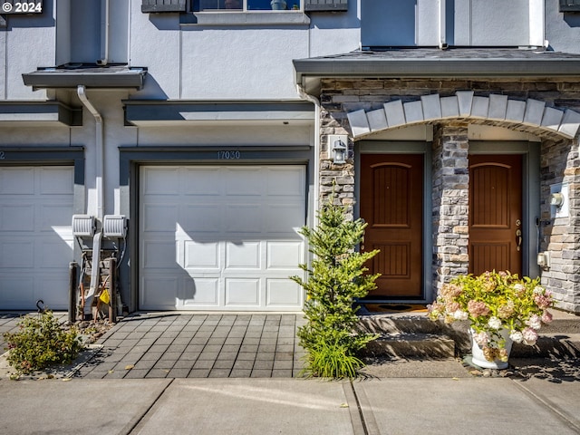 property entrance featuring decorative driveway, a garage, stone siding, and stucco siding