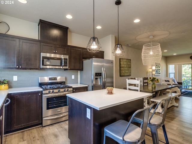 kitchen with backsplash, a center island, light wood-type flooring, appliances with stainless steel finishes, and dark brown cabinetry