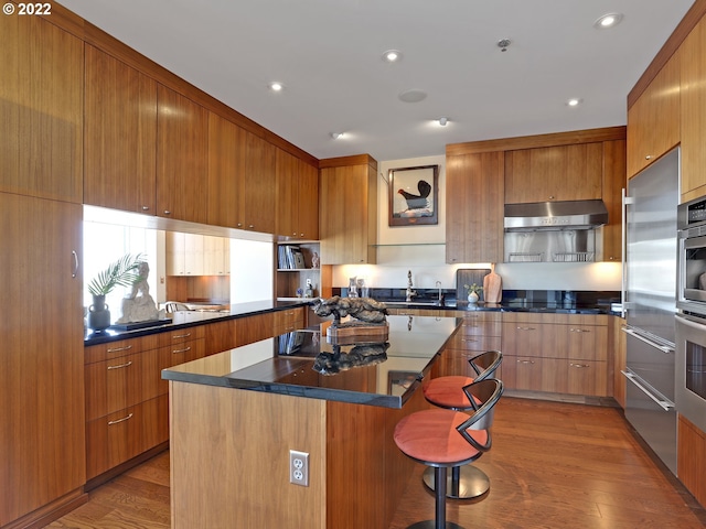 kitchen with sink, cooktop, hardwood / wood-style floors, a breakfast bar area, and a kitchen island