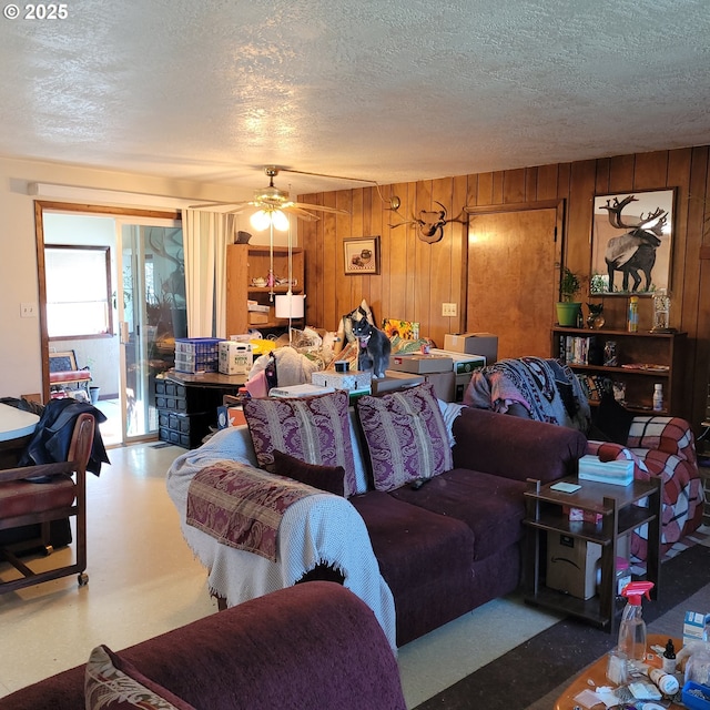 living area featuring wood walls, a textured ceiling, and a ceiling fan