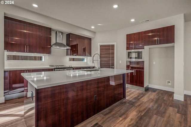 kitchen featuring sink, stainless steel appliances, wall chimney exhaust hood, dark hardwood / wood-style floors, and a kitchen island with sink