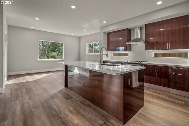 kitchen featuring a breakfast bar area, a kitchen island with sink, light wood-type flooring, wall chimney exhaust hood, and sink