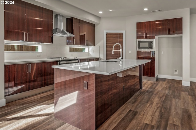 kitchen featuring appliances with stainless steel finishes, sink, dark hardwood / wood-style flooring, wall chimney exhaust hood, and a center island with sink