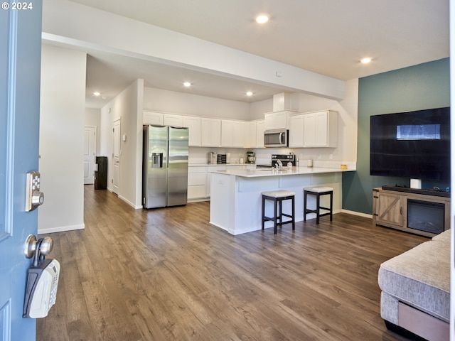 kitchen featuring white cabinetry, dark hardwood / wood-style flooring, kitchen peninsula, a kitchen bar, and appliances with stainless steel finishes