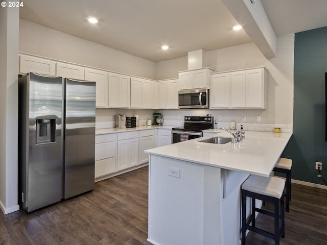 kitchen with sink, appliances with stainless steel finishes, white cabinetry, dark hardwood / wood-style flooring, and kitchen peninsula