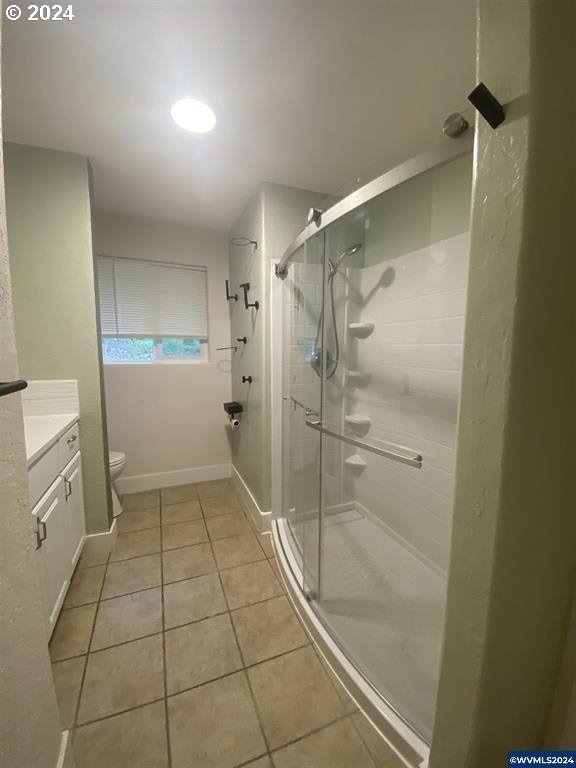 bathroom featuring toilet, tile patterned flooring, vanity, and a shower with shower door