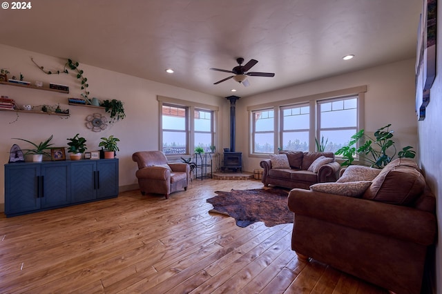 living room with a wood stove, light wood-type flooring, and ceiling fan