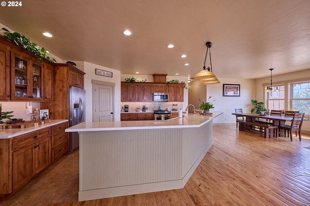 kitchen featuring light hardwood / wood-style floors, stainless steel appliances, hanging light fixtures, and a large island with sink