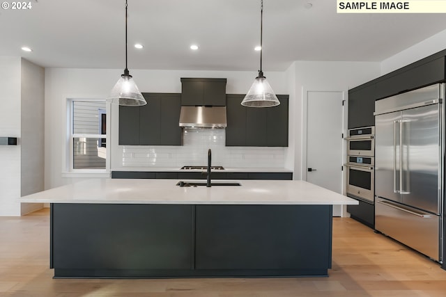 kitchen with stainless steel appliances, an island with sink, pendant lighting, light wood-type flooring, and range hood