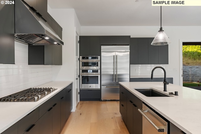 kitchen with stainless steel appliances, a sink, under cabinet range hood, decorative light fixtures, and light countertops