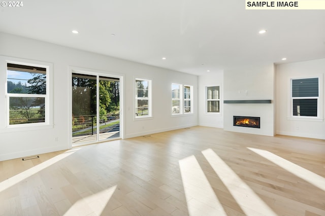 unfurnished living room featuring a glass covered fireplace, recessed lighting, light wood-style floors, and baseboards