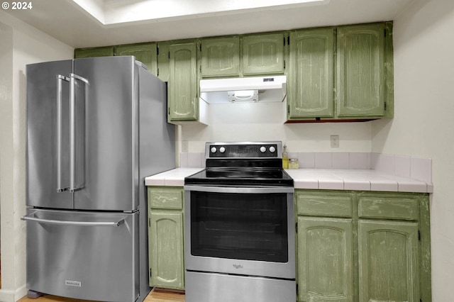 kitchen with tile countertops, stainless steel appliances, green cabinets, and light hardwood / wood-style floors