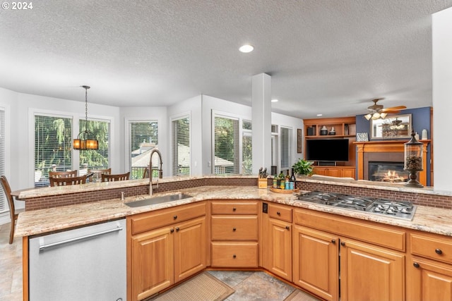 kitchen with stainless steel appliances, a glass covered fireplace, a healthy amount of sunlight, a sink, and light stone countertops