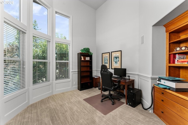 office space featuring a towering ceiling, a wainscoted wall, a decorative wall, and light colored carpet