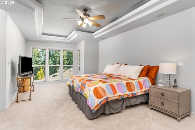 bedroom with a tray ceiling, light carpet, ceiling fan, and a textured ceiling