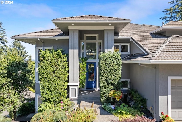 property entrance with a garage, a tile roof, and stucco siding