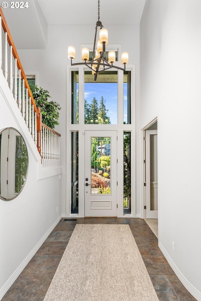 foyer entrance with a chandelier, stone finish floor, a high ceiling, and baseboards