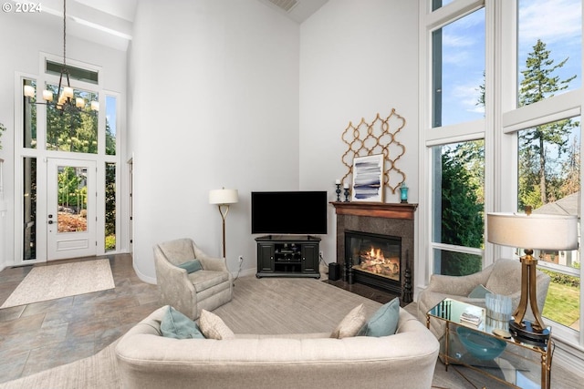 living room featuring baseboards, a tile fireplace, a towering ceiling, stone finish flooring, and a notable chandelier