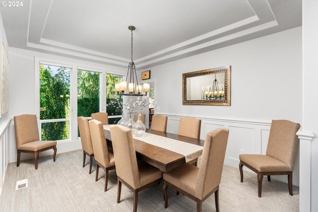 dining space with a tray ceiling, light colored carpet, a decorative wall, and visible vents