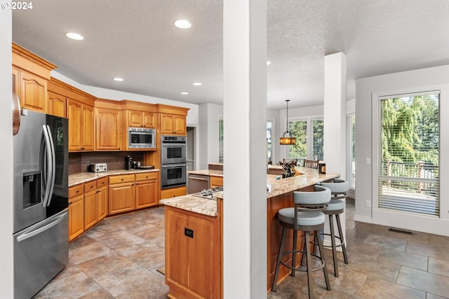 kitchen featuring a textured ceiling, light stone counters, recessed lighting, a kitchen breakfast bar, and appliances with stainless steel finishes