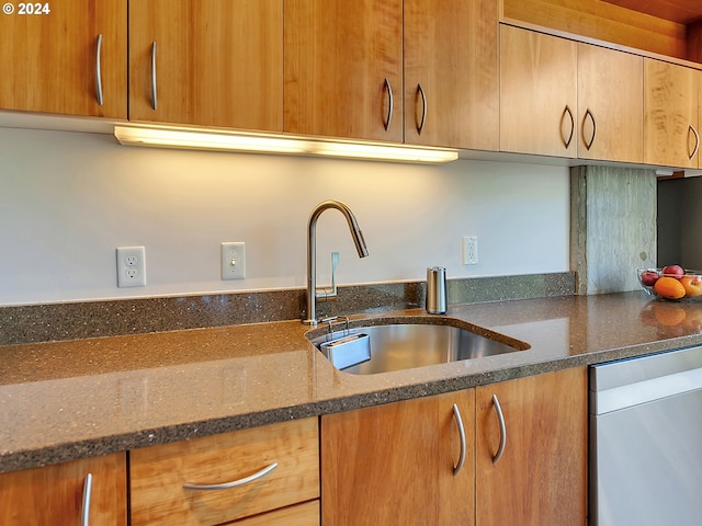 kitchen featuring stainless steel dishwasher, dark stone countertops, and sink