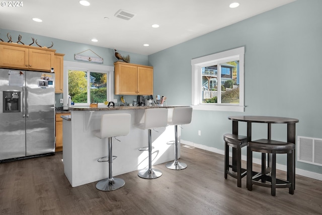 kitchen featuring a kitchen bar, stainless steel fridge with ice dispenser, a wealth of natural light, and dark hardwood / wood-style flooring