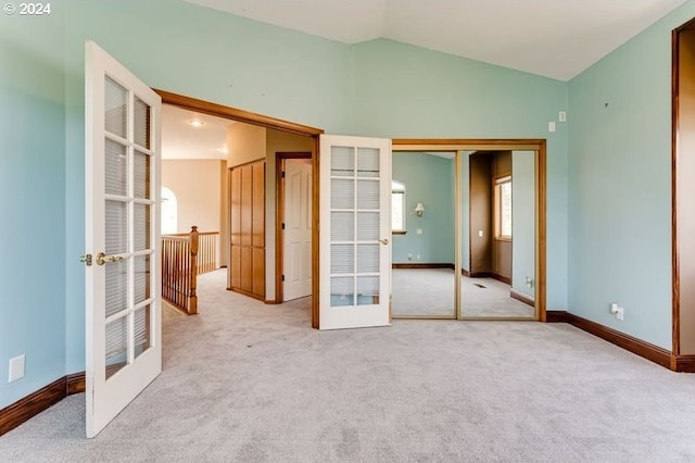 unfurnished bedroom featuring light carpet, a closet, vaulted ceiling, and french doors