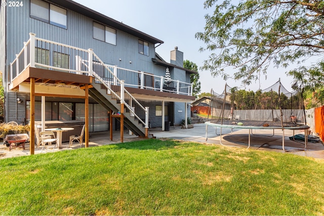 back of house with a patio, a wooden deck, a trampoline, and a lawn