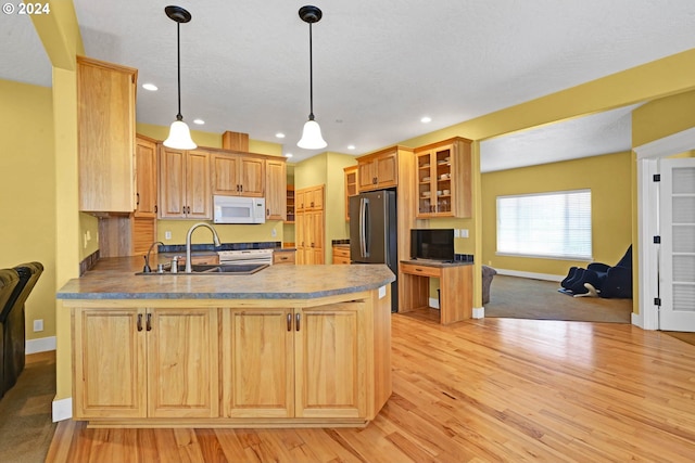 kitchen with sink, stainless steel refrigerator, kitchen peninsula, pendant lighting, and light hardwood / wood-style floors